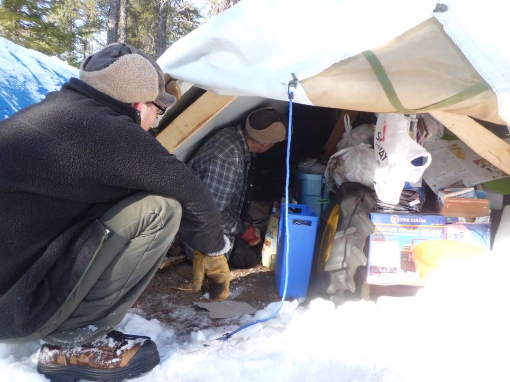 Two men crouched by a collapsed tent in winter.
